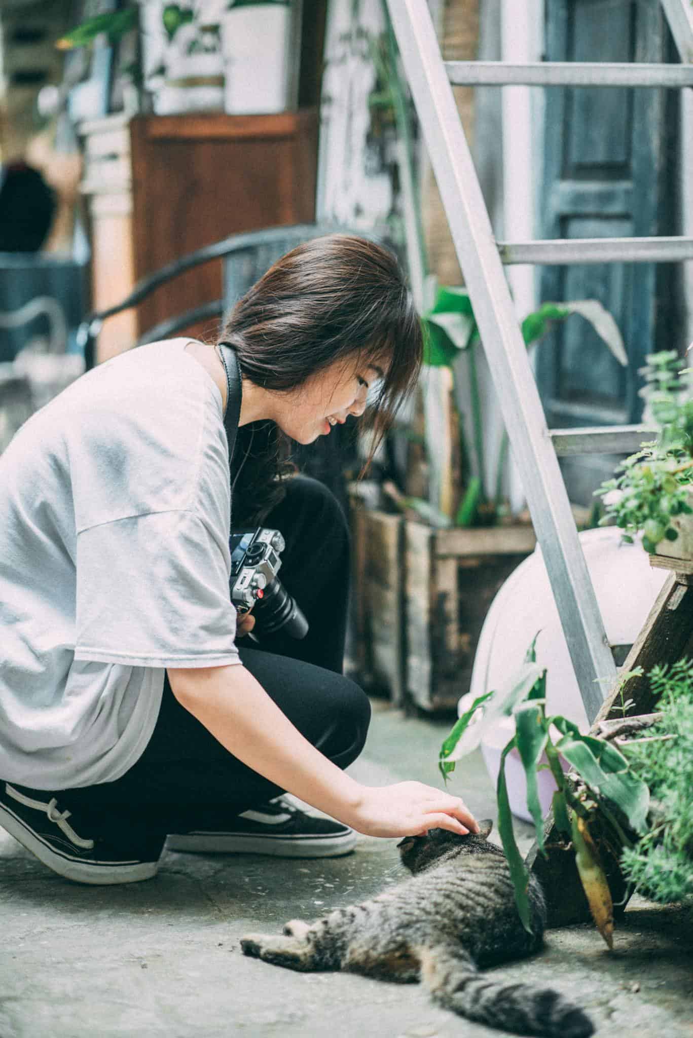 About Young woman strokes a cat amidst plants and urban decor, capturing an intimate city moment.